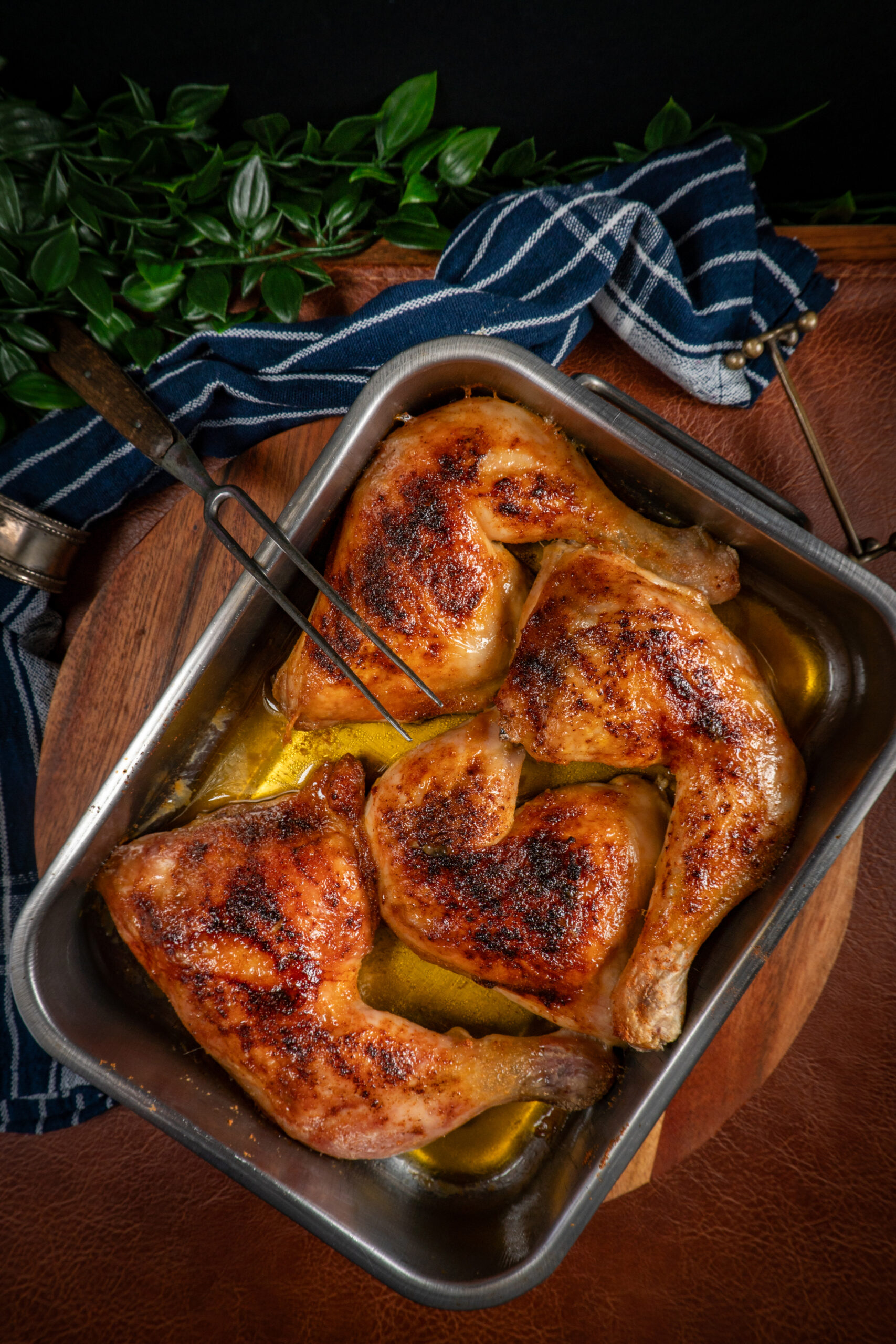 Baked chicken legs in metal baking dish on a wooden kitchen board.