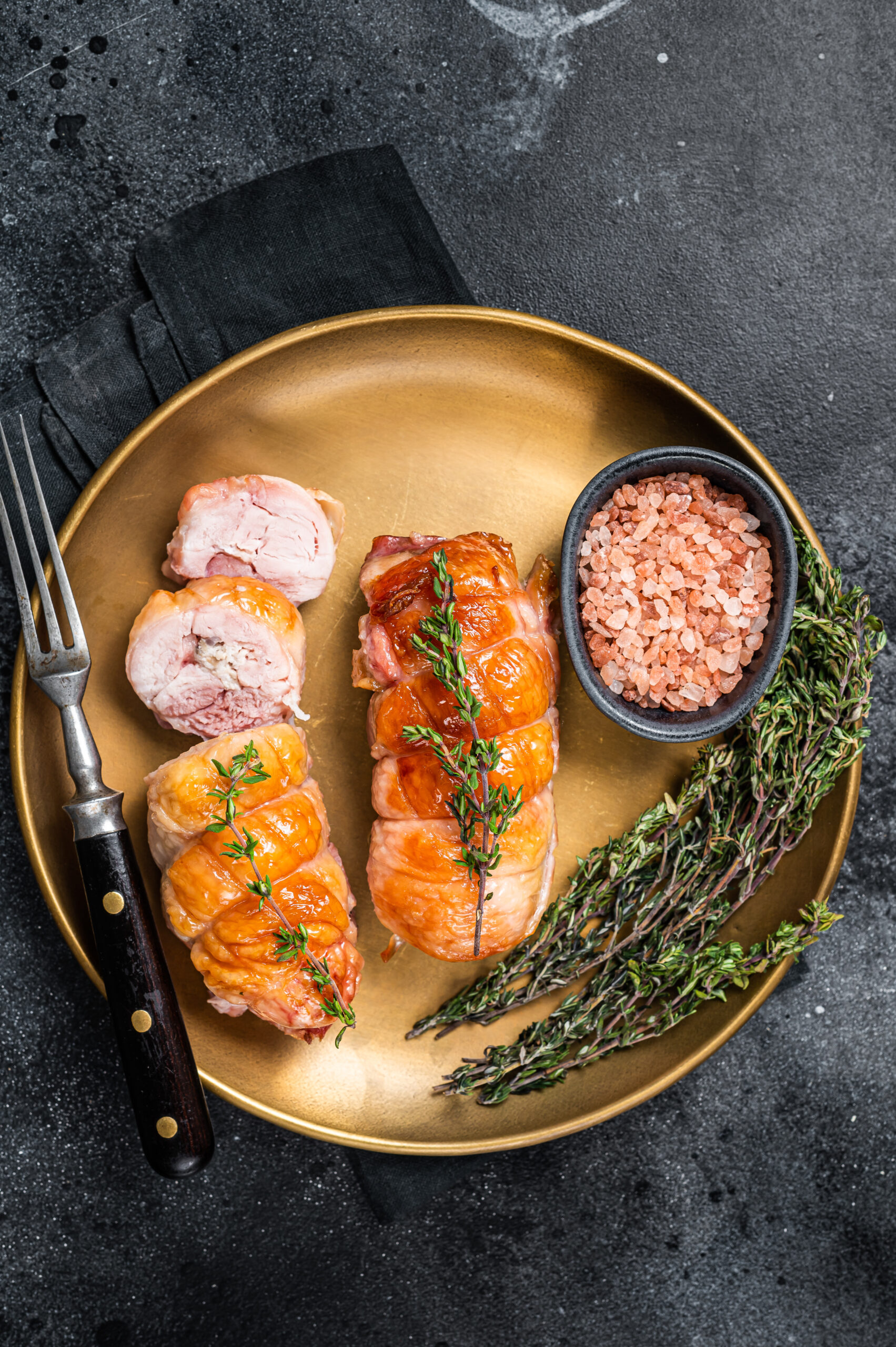 Roasted Stuffed chicken roll with cheese and ham on a steel plate. Dark background. Top view.