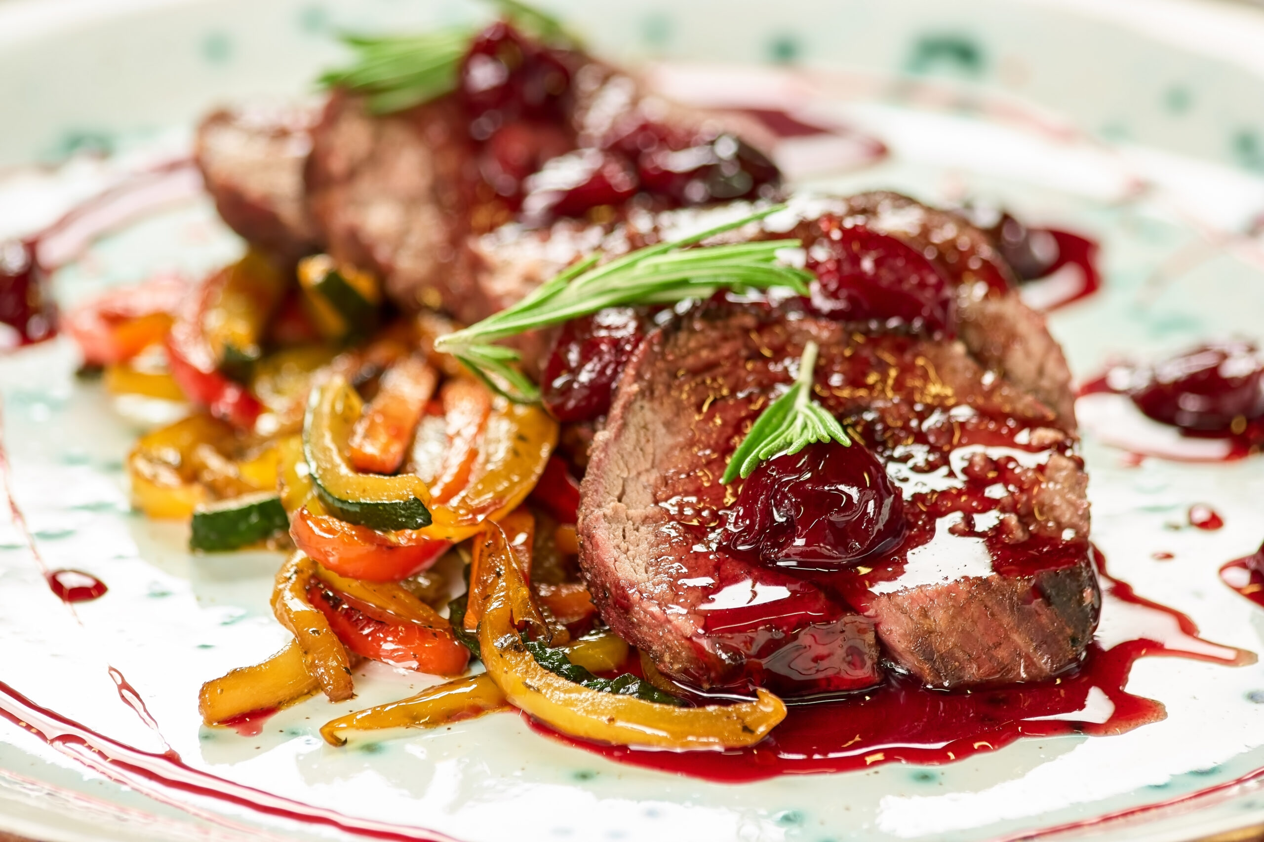 Veal with cherry sauce and vegetables. Dish with cherry sauce, rosemary and sliced vegetables on a plate.